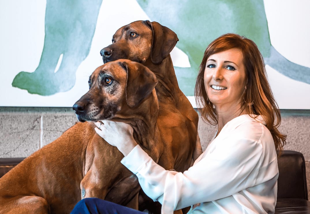 Founder and Chief Integrity Officer, Lucy Postins, sitting on a couch with two large dogs