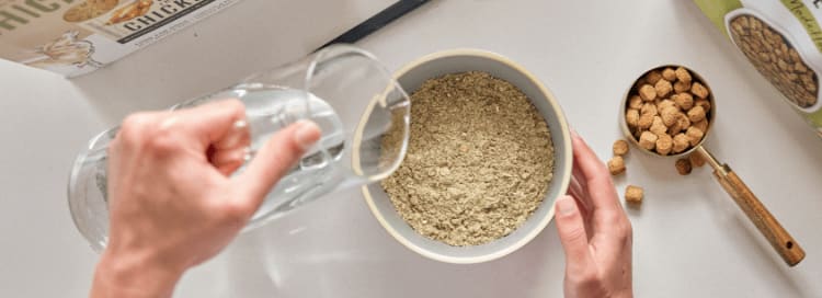 A woman in the kitchen pouring water into her pet’s bowl filled with The Honest Kitchen food in it.