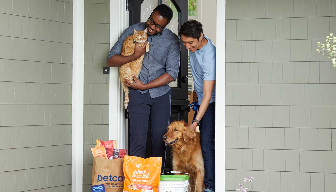 Two men with a cat and a dog answering the door to receive a Petco order.