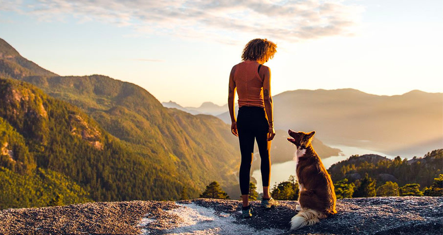 Dog and owner standing on a ledge overlooking a river running between mountains.